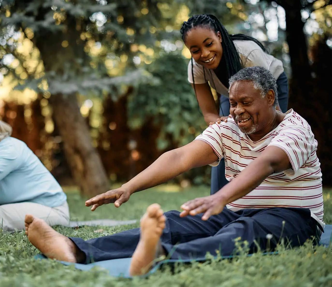 A cheerful black physical therapist is helping seniors during an exercise class in the park