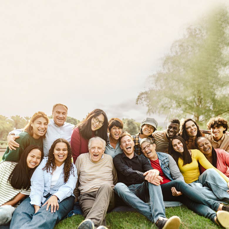A group of multigenerational caregivers is sitting on the grass in a public park having a great time and feeling happy
