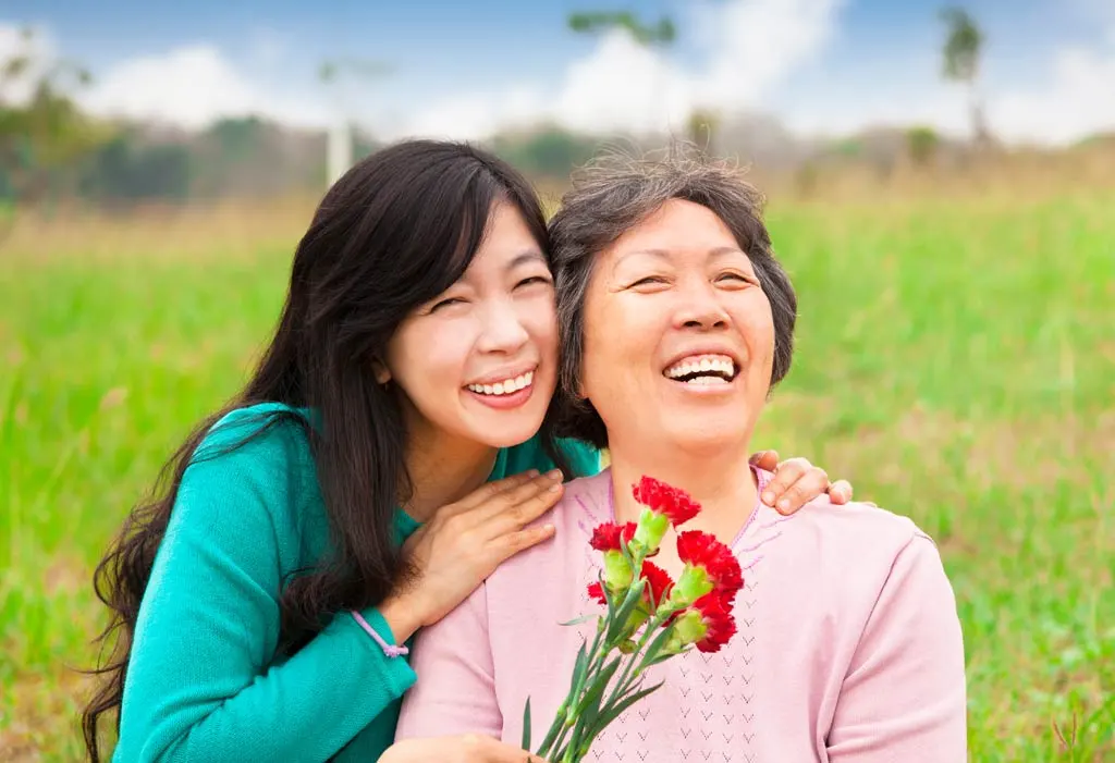 The smiling caregiver and her elderly women held carnation flowers on the grassy field
